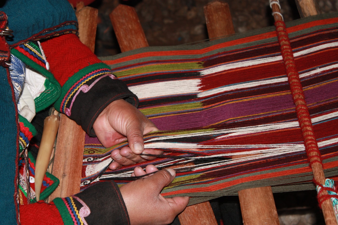 Manos tejiendo una pieza de colores en un telar de madera